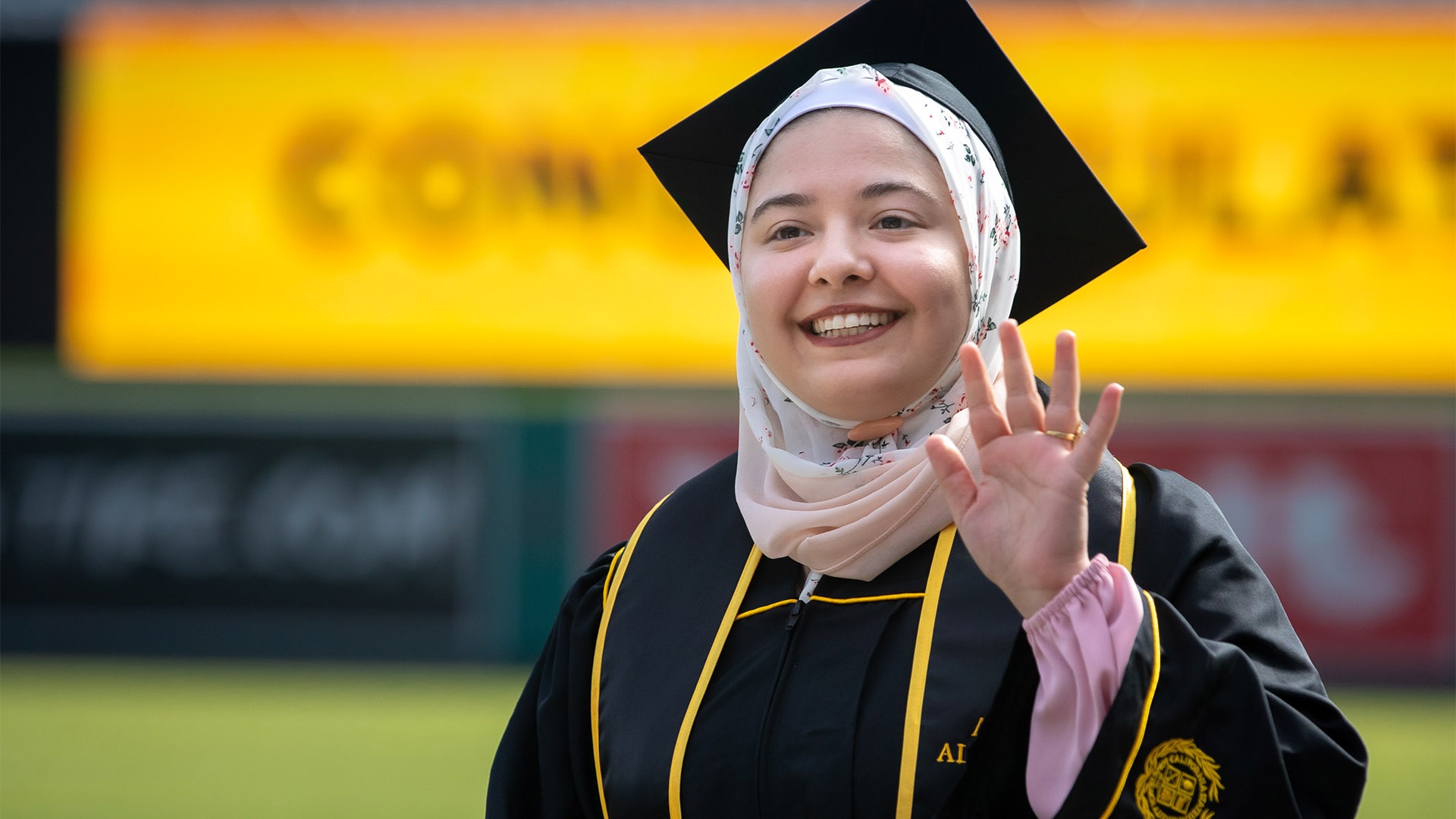 Female graduate wearing a hijab waves to the Commencement cr