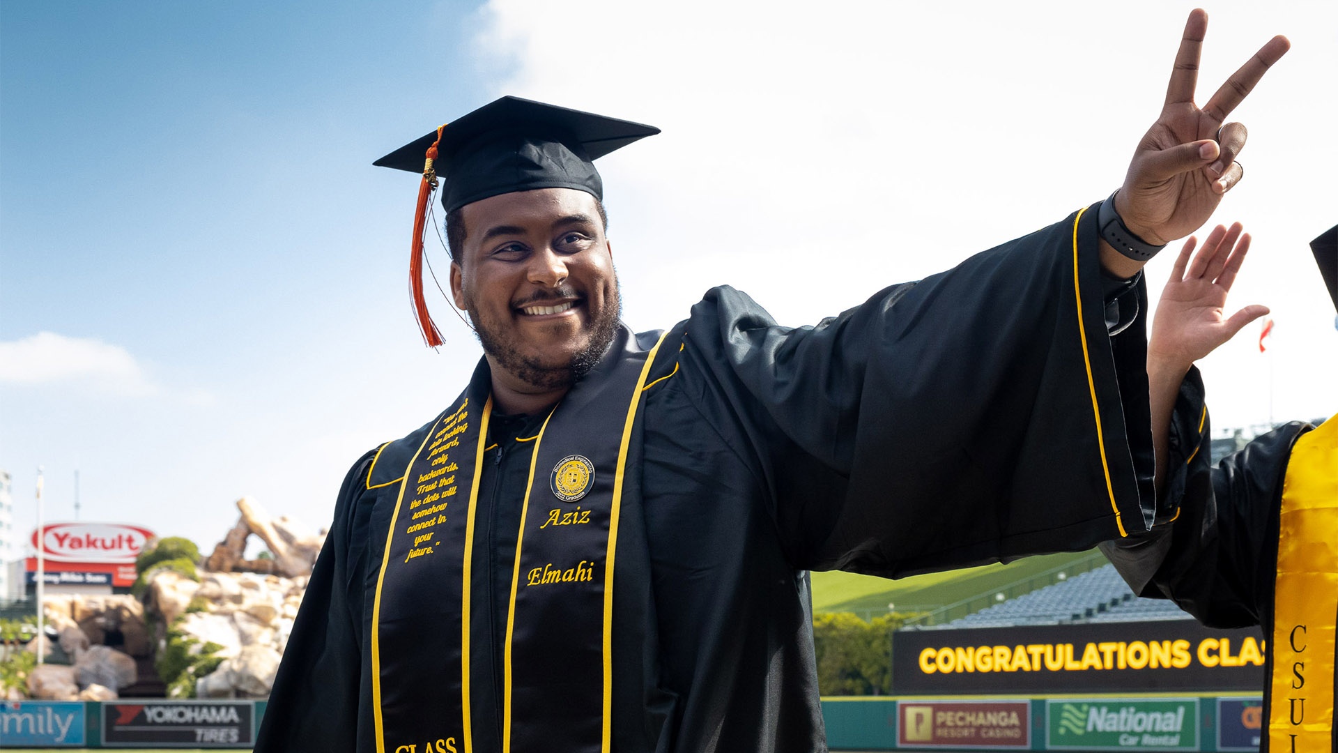 A smiling College of Engineering graduate flashes a piece si