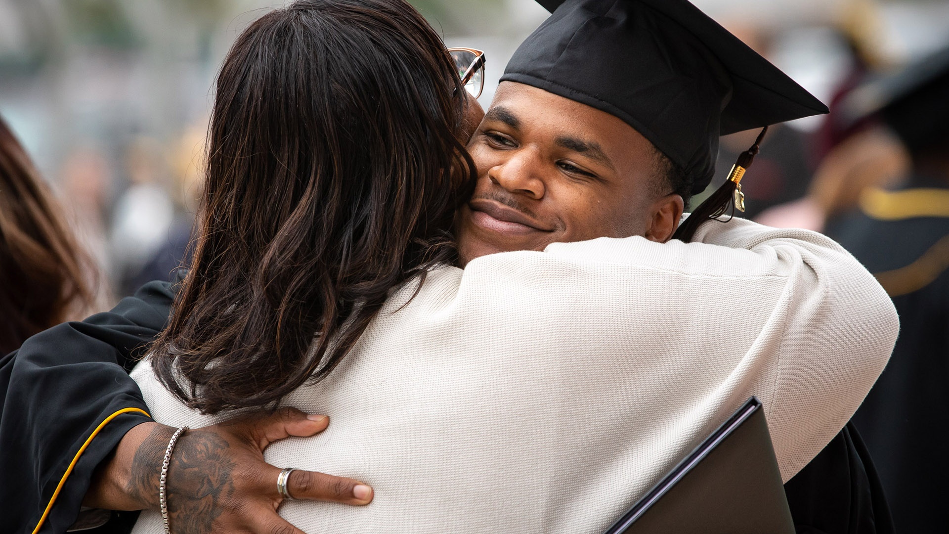 commencement-cota-hero3.jpg Male graduate hugs a friend after Commencement ceremonies.