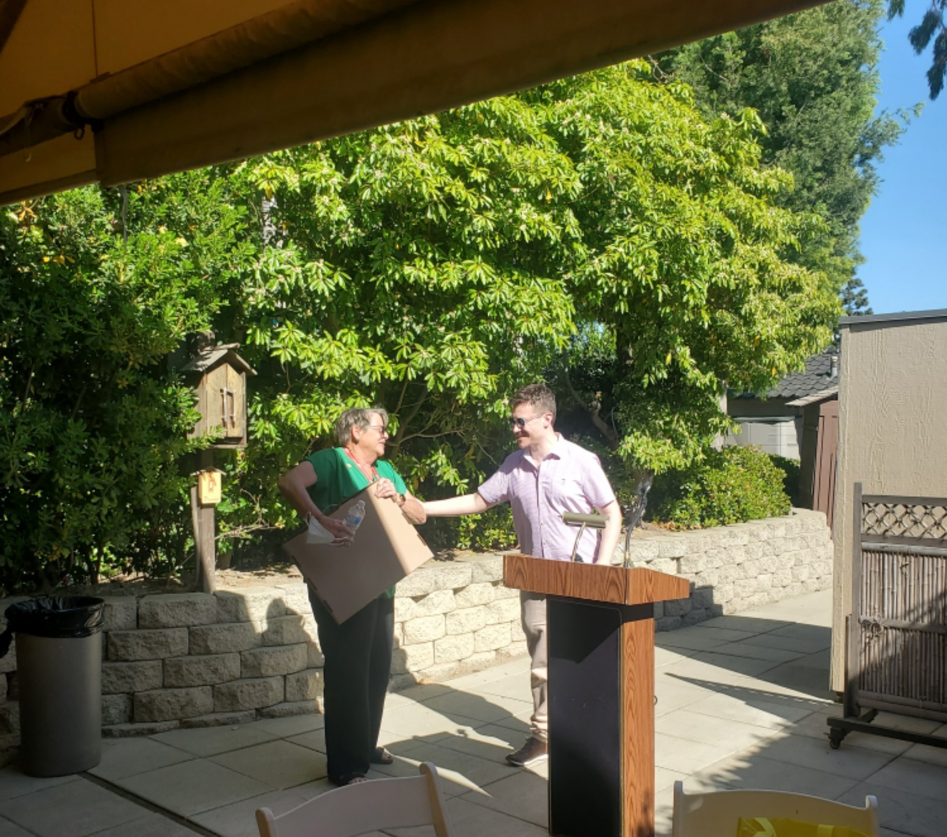 Two people are smiling and standing next to a podium. One pe