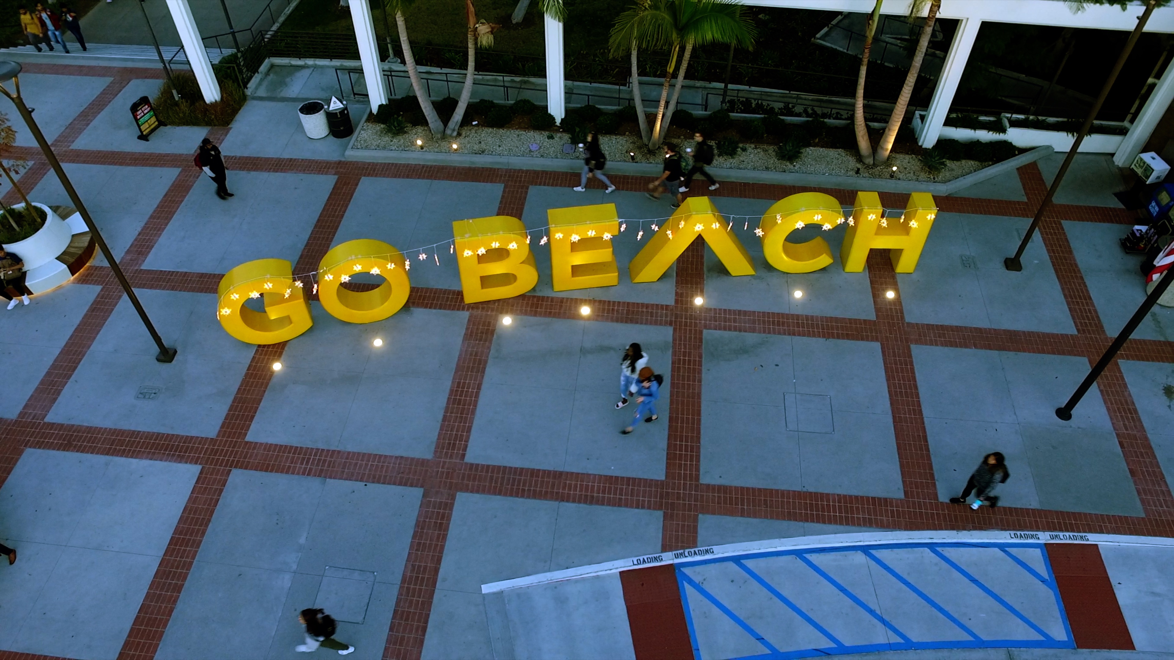 Students walk past the Go Beach sign adorned with holiday lights.