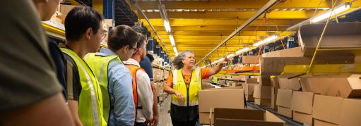 A tour guide explaining supply chain operations to students standing near a conveyer moving boxes
