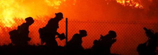 Five firefighters walk around the perimeter of a growing fire