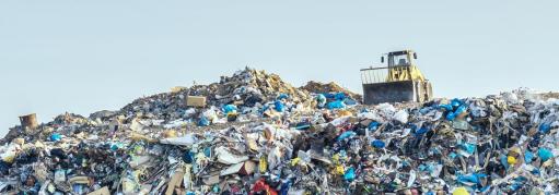 A landfill compactor drives on top of a massive landfill. 
