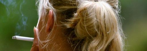 A blonde woman with her face turned away smokes a cigarette. 