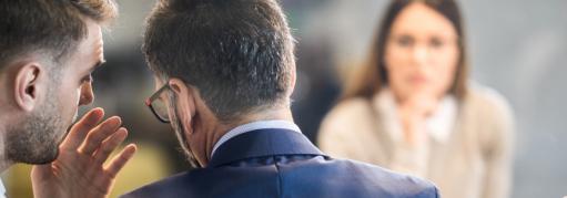 A business man whispers to a male associate in front of two other colleagues.