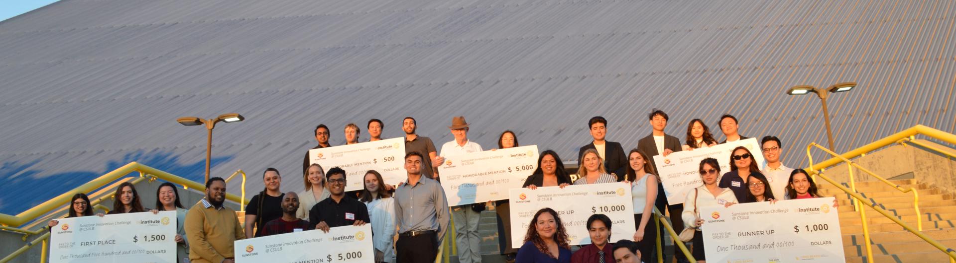 group of people posting in front of pyramid on stairs with jumbo checks