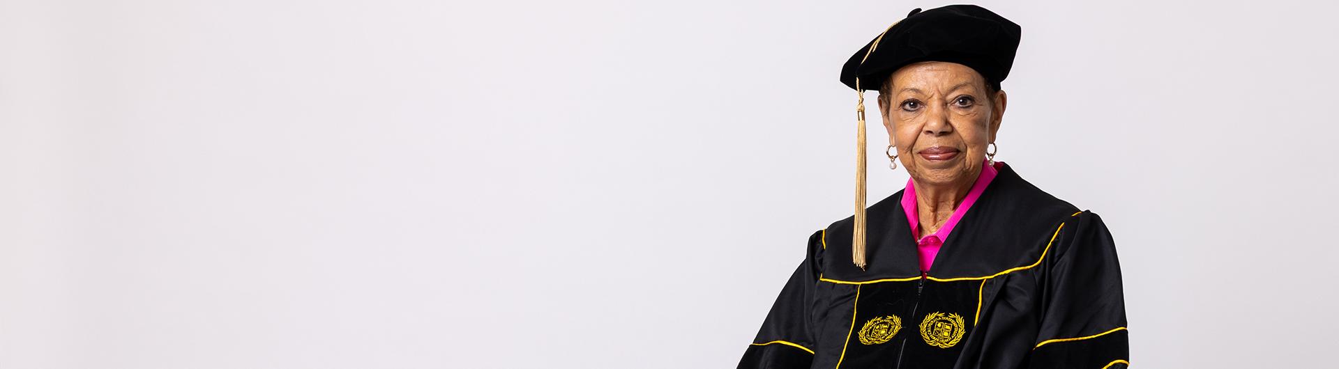 A person wearing academic regalia with embroidered seals sits facing forward