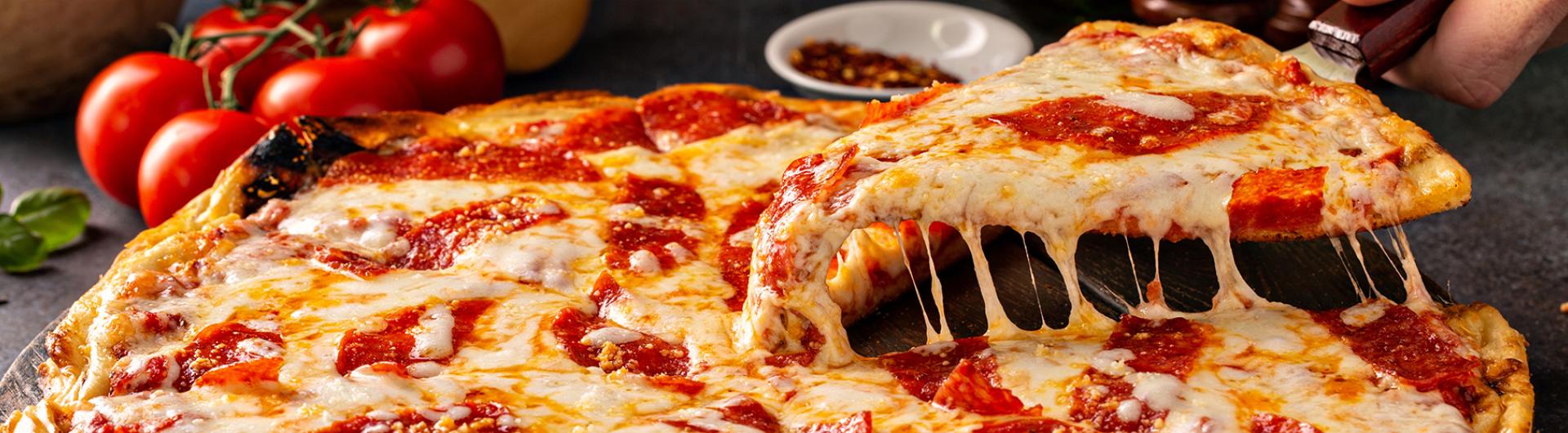 A slice of pepperoni pizza being lifted up showing the cheese pull from the rest of the pizza. 