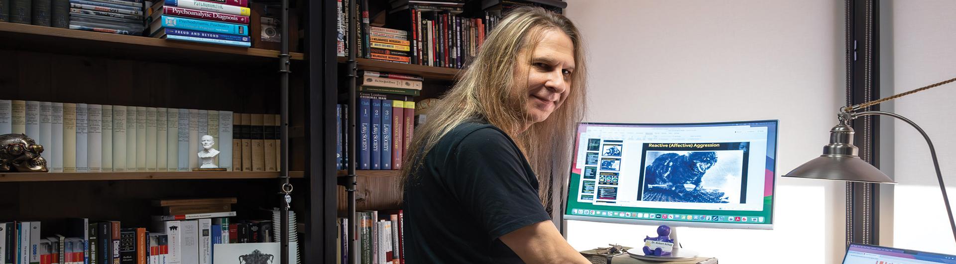 Man with long hair in front of computer, looking back toward camera