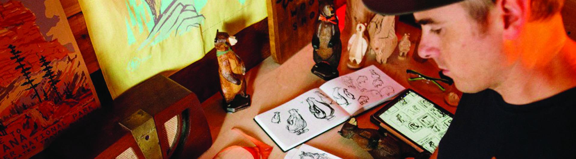 A person stands over a desk drawing cartoons characters