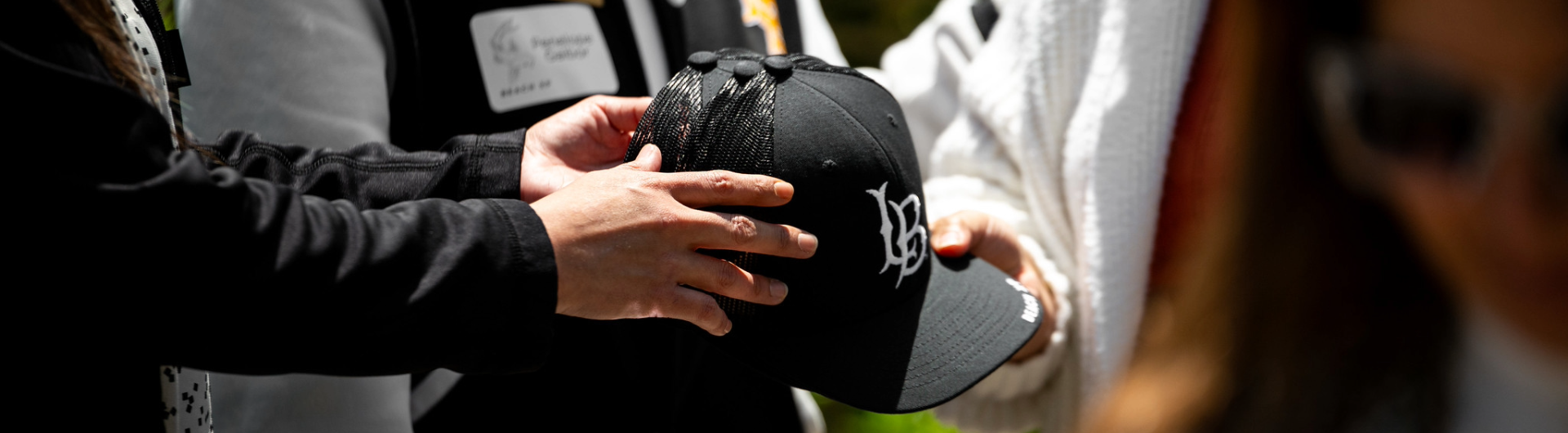 hands carrying a black hat with an LB logo