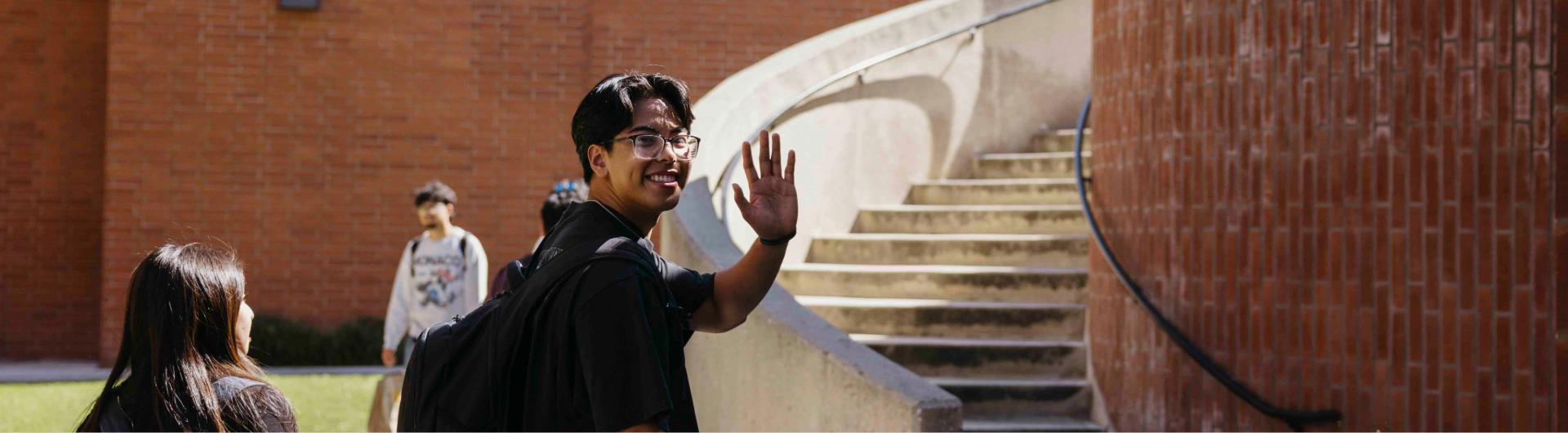 A student smiles and waves to the camera