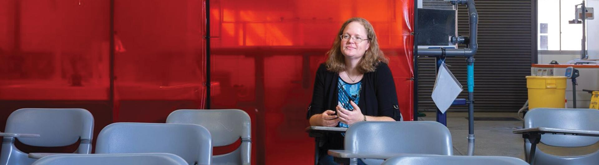 A person sits smiling at a desk in a classroom 