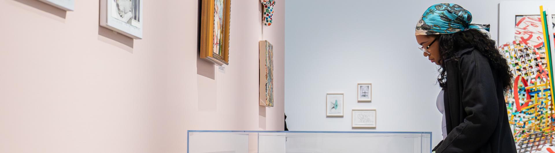 A person viewing a display of artwork behind a glass case