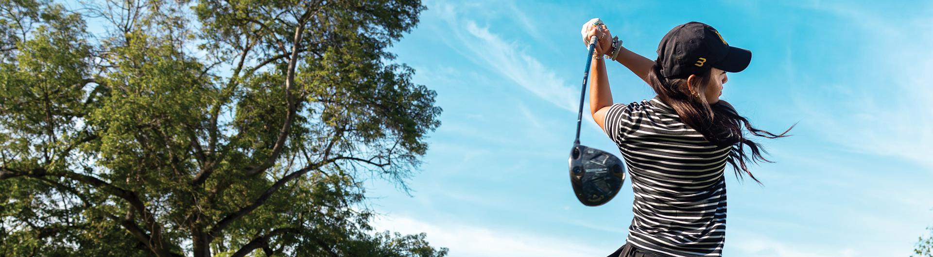 A person follows through on a golf swing under a blue sky.