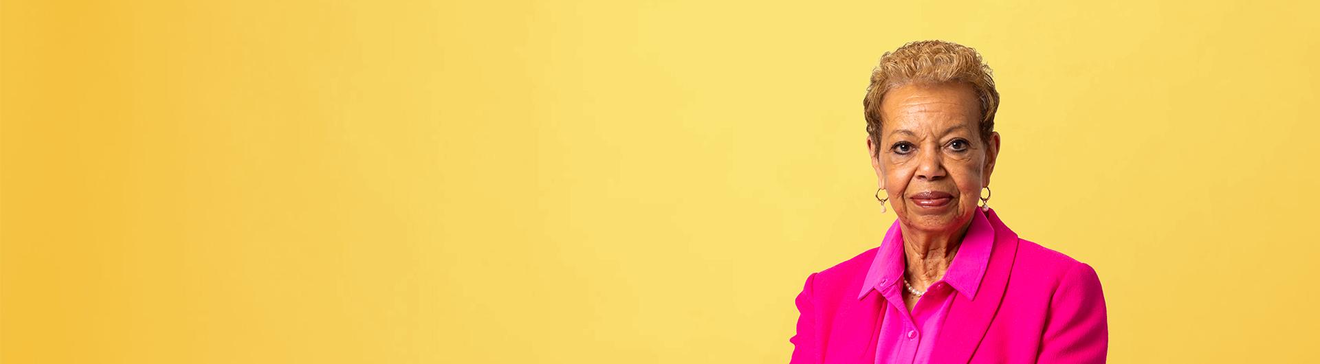 Person wearing pink faces camera with yellow background
