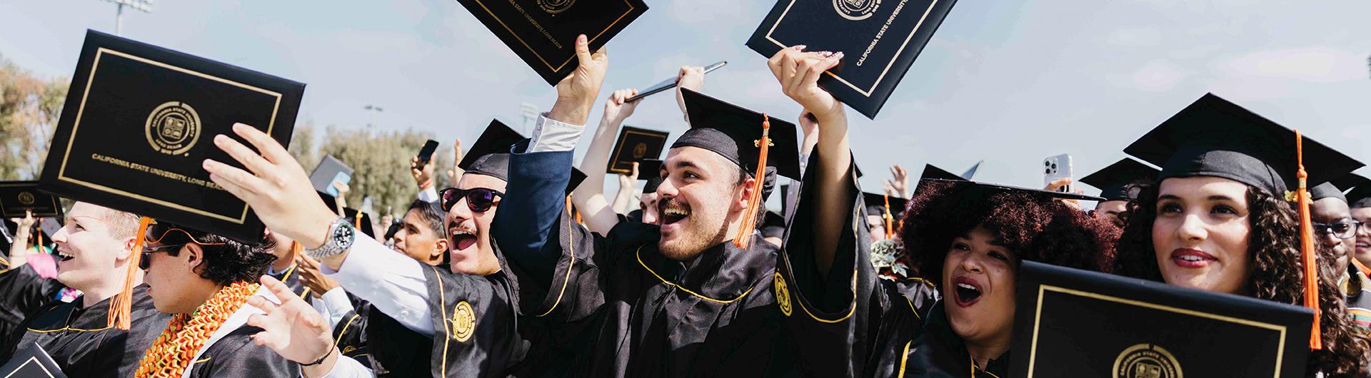 CSULB graduates holding up their diplomas