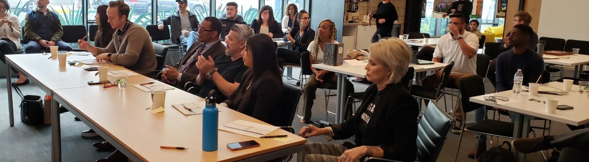 diverse group of people sitting all looking at the front of the room