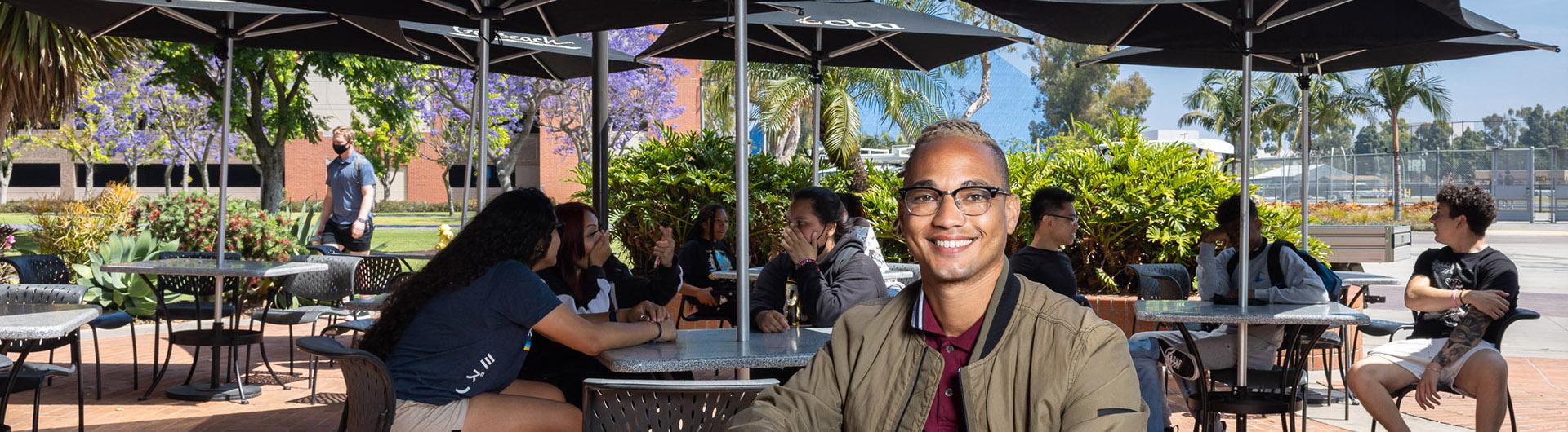 CSULB alumnus Austin Metoyer sits at a picnic table and smiles at the camera.
