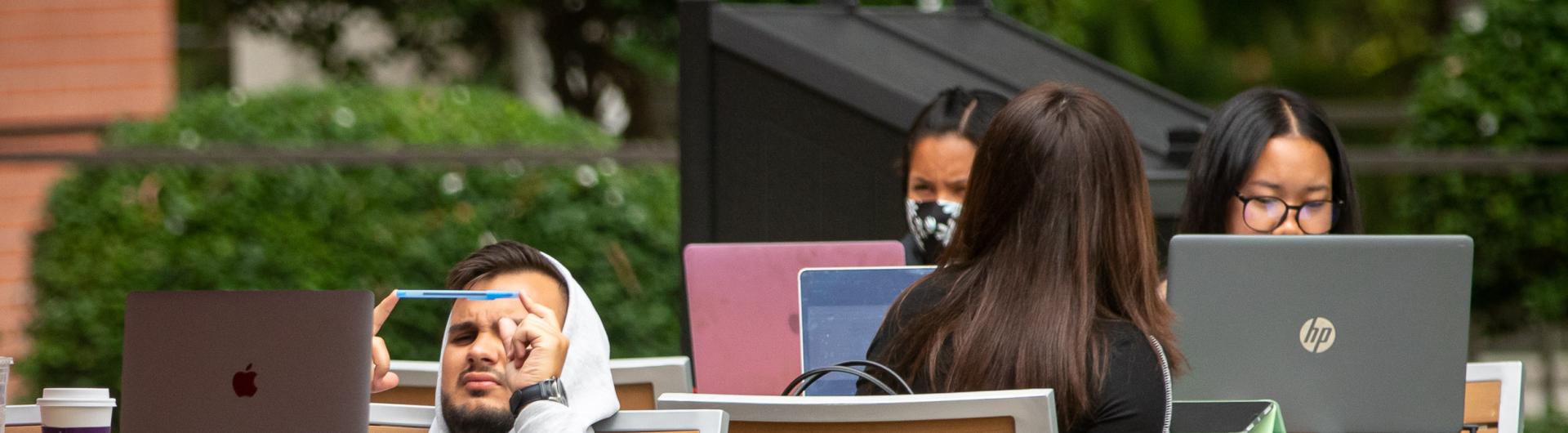 Students sitting with laptops in chairs outside wit