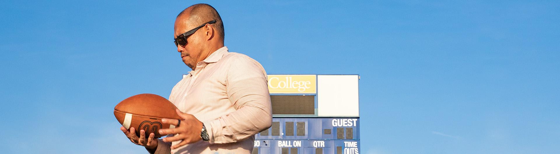 Alumnus Junior Domingo holds a football 