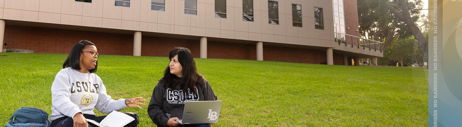 Students sit on grass while working on computers