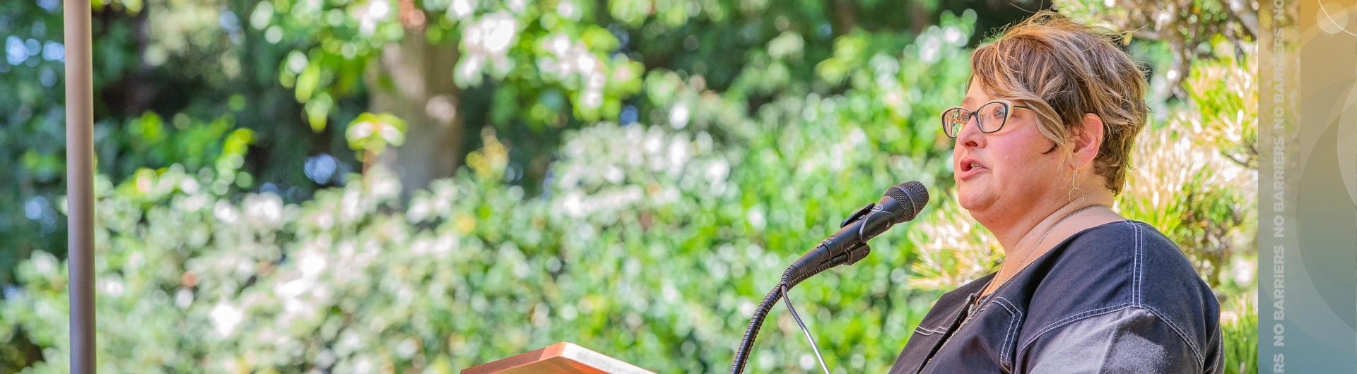 Professor Beth Manke speaking at podium under an umbrella