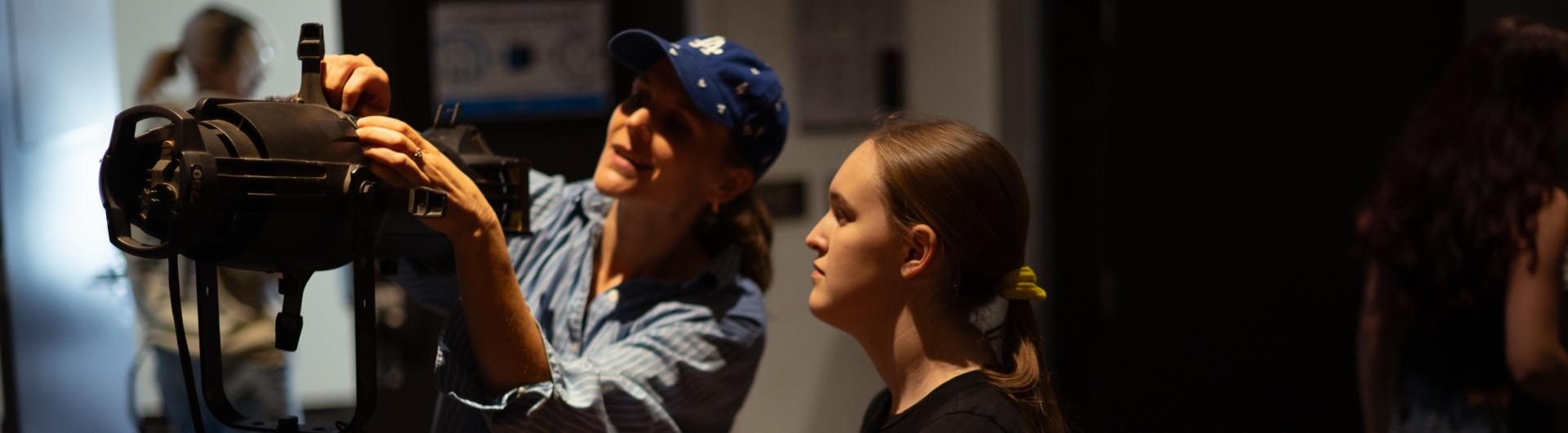 Theatre Arts faculty member assists a student with a lighting instrument.