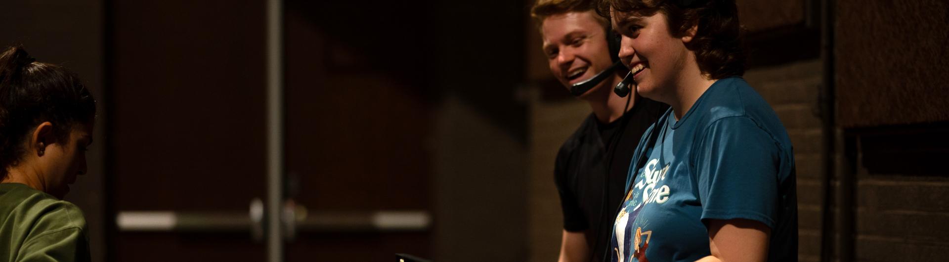 Two students with headsets on smile while they talk