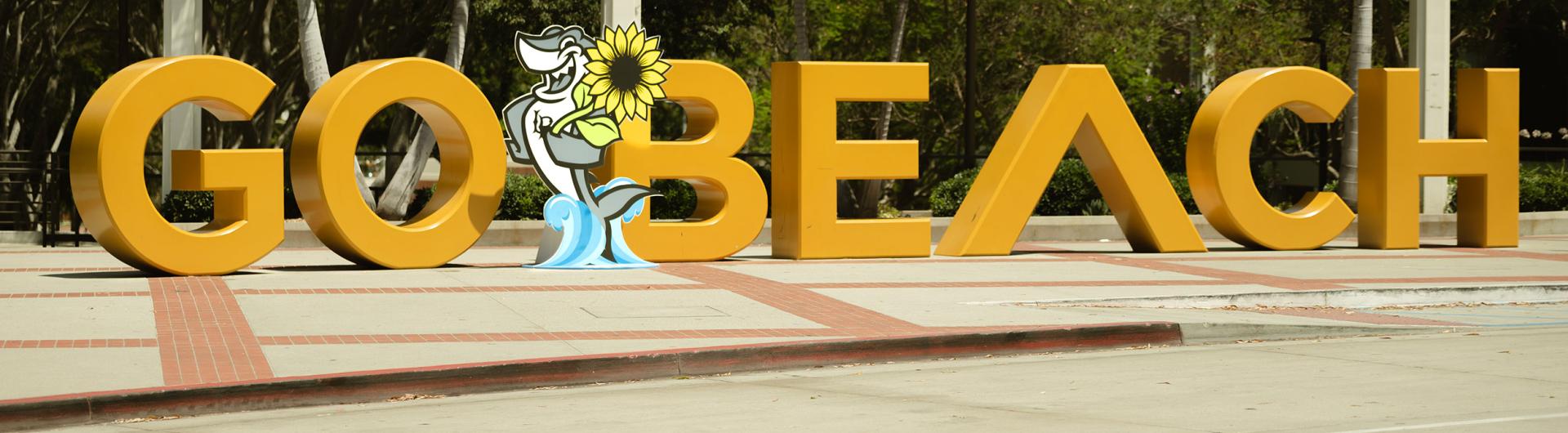 Elbee with a sunflower in front of Go Beach sign