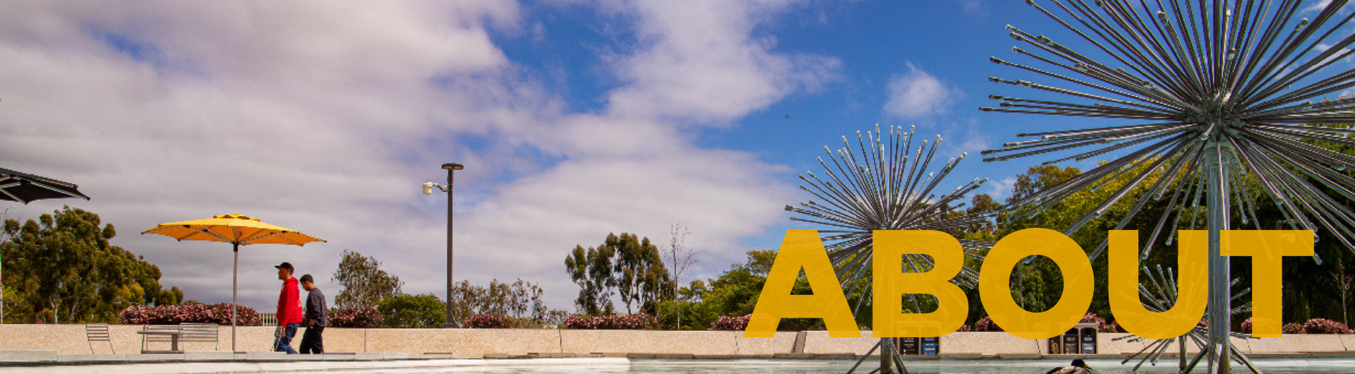 The image shows two people walking outside near the CSULB Brotman Hall fountain, with yellow umbrellas and a partly cloudy sky. The word "ABOUT" is overlaid in bold yellow letters on the right side.