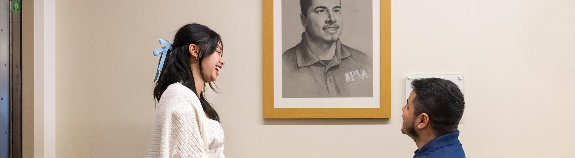 Carina Tan, left, and Jose Reynoso in front of veteran's portrait