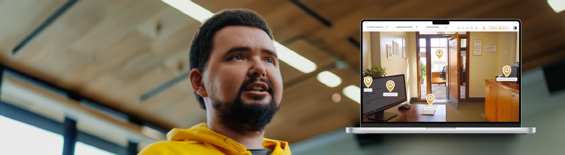 person in a yellow hoodie in a classroom with a computer with a simulation game on it