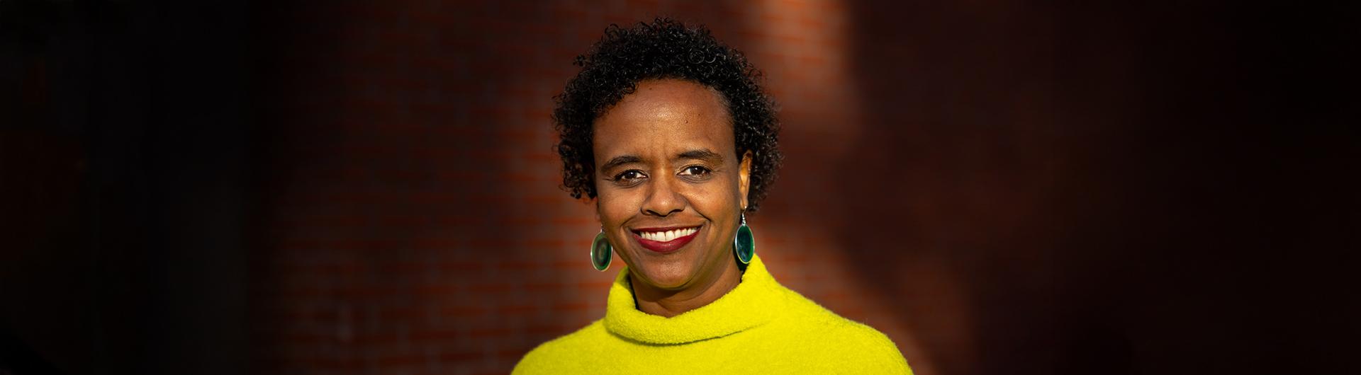 Professor Rashida Crutchfield smiling and wearing a yellow sweater.