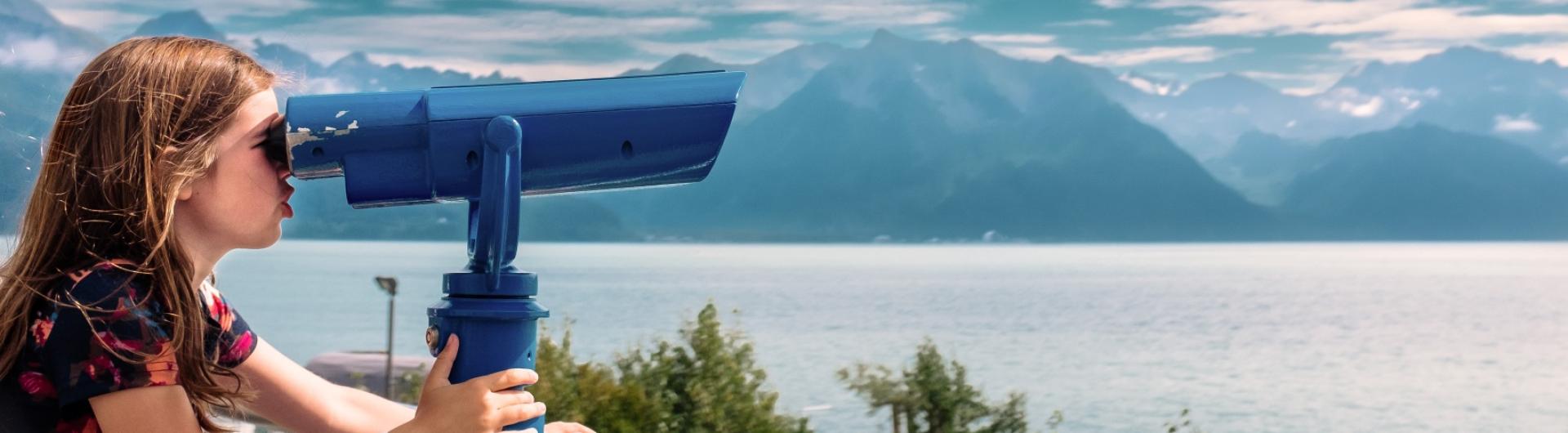 A young girl looks through tourist binoculars toward a fjord in Alaska