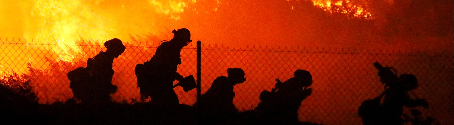 Five firefighters walk around the perimeter of a growing fire