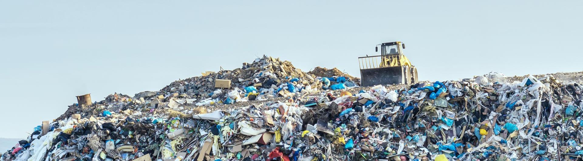 A landfill compactor drives on top of a massive landfill. 