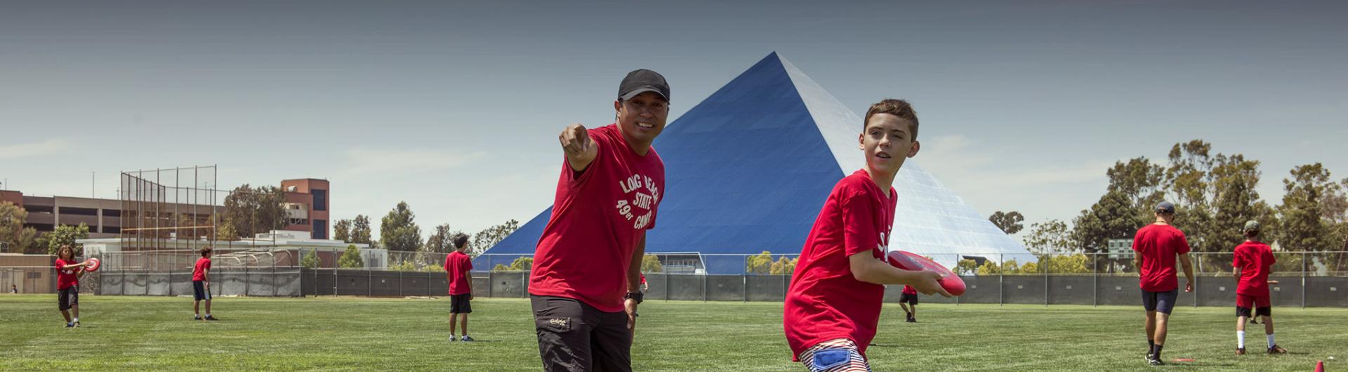 Page banner: young students playing ball on campus field, pyramid is seen in the background.