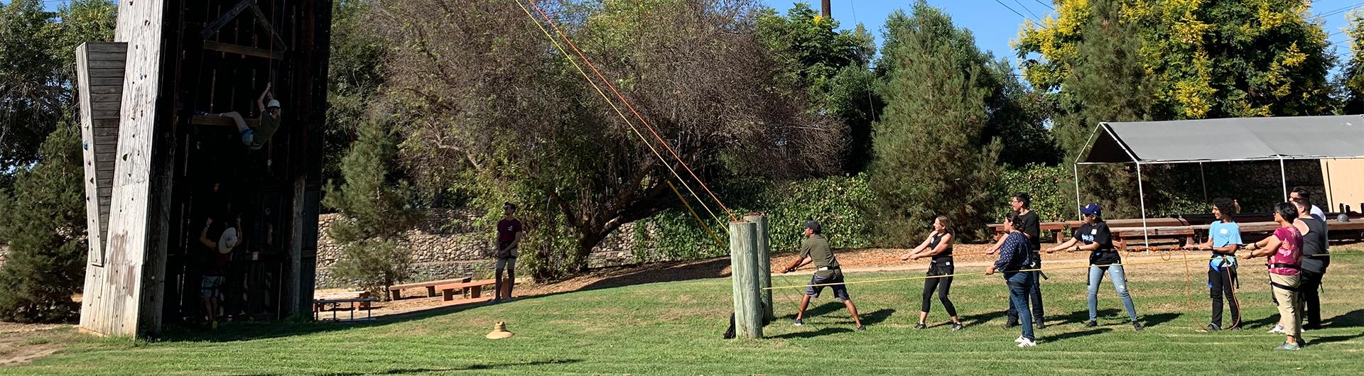 students holding rope to help others scale up a wall