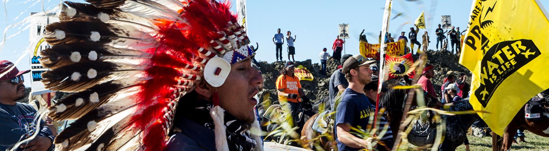 A Couchiching First Native citizen, wearing a war bonnet, stands with other members against the Dakota Access Pipeline.