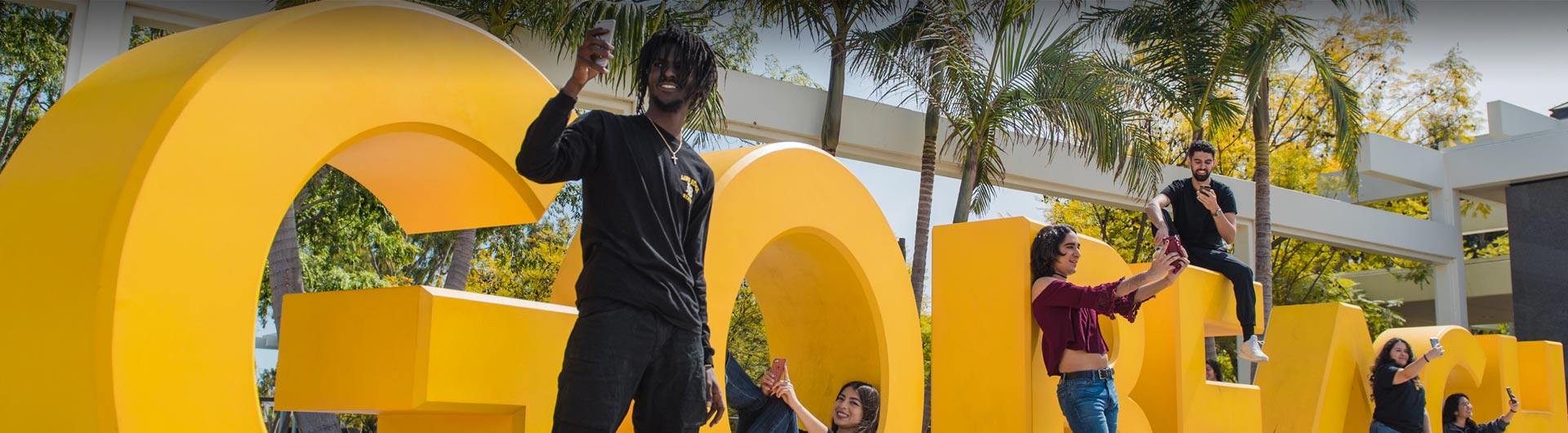 Students taking selfies at the "go beach" sign