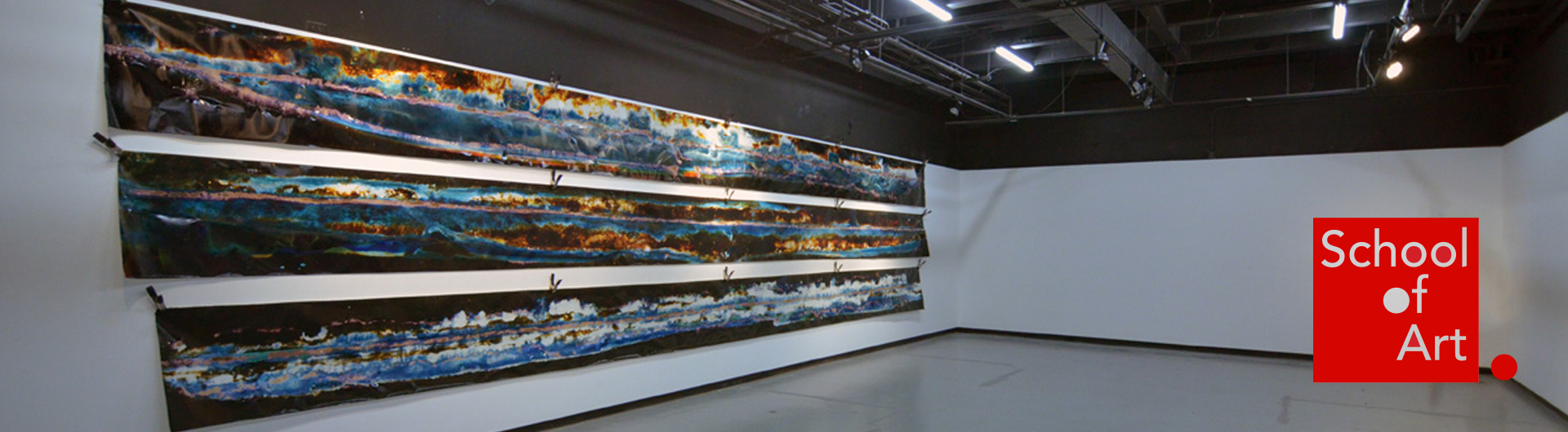 Three large, colorful fabric panels displayed atop one another on a gallery wall