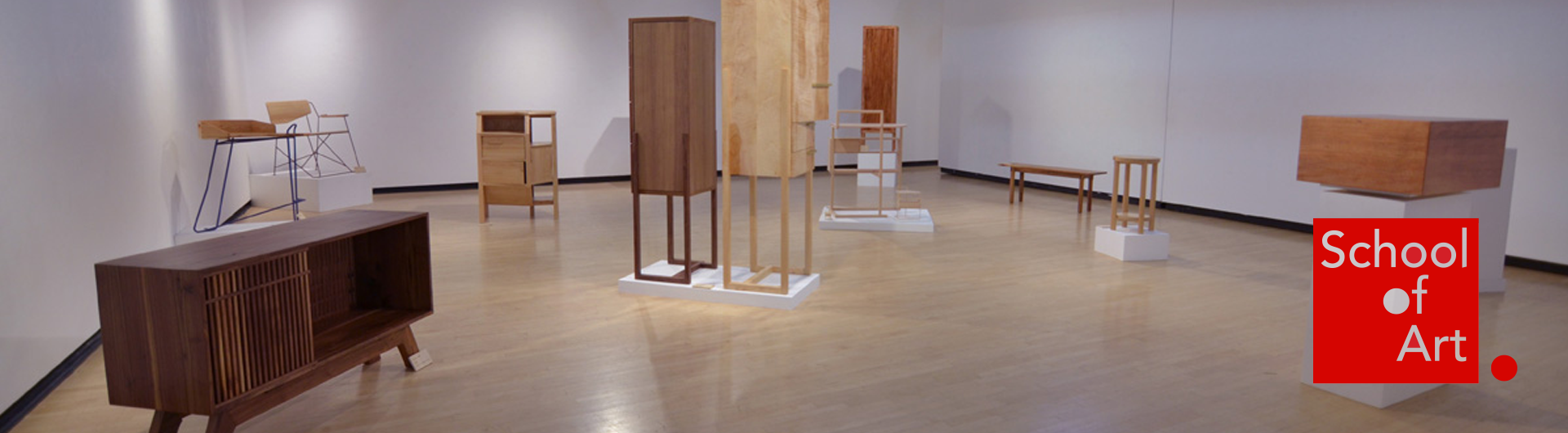 Student wood projects, including cabinets, tables and chairs, arranged in a gallery exhibit