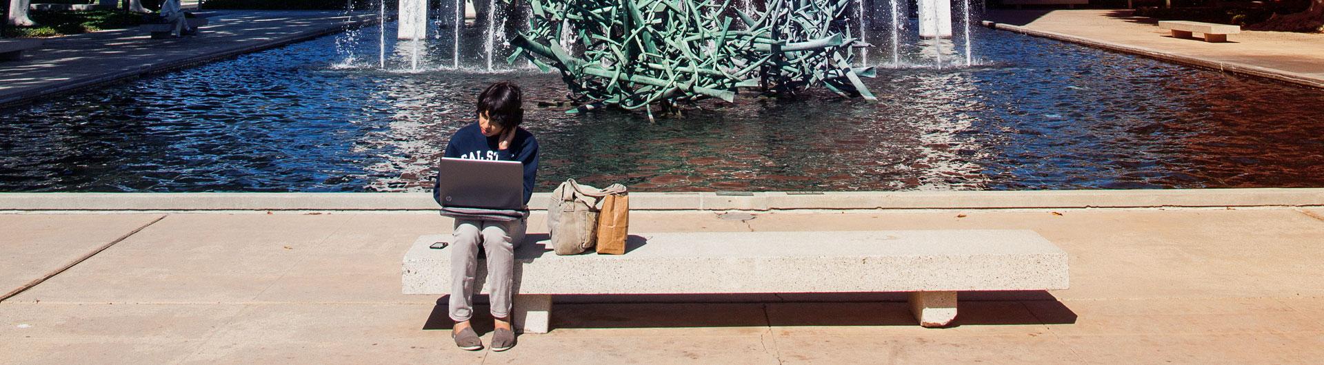 Student on his laptop by the Macintosh building water fountain