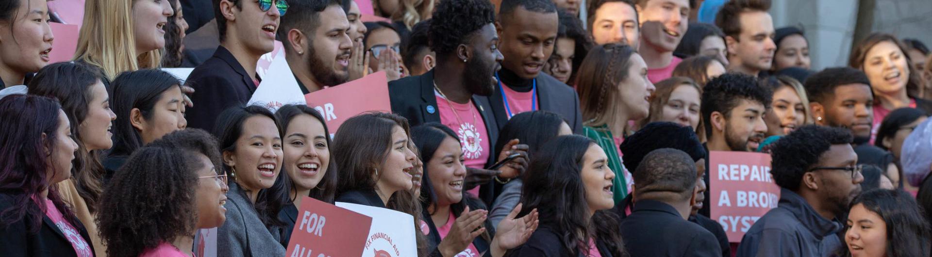 Students in a large group with signs about grants