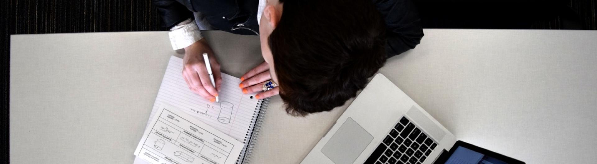 Student writes on white paper on a white desk