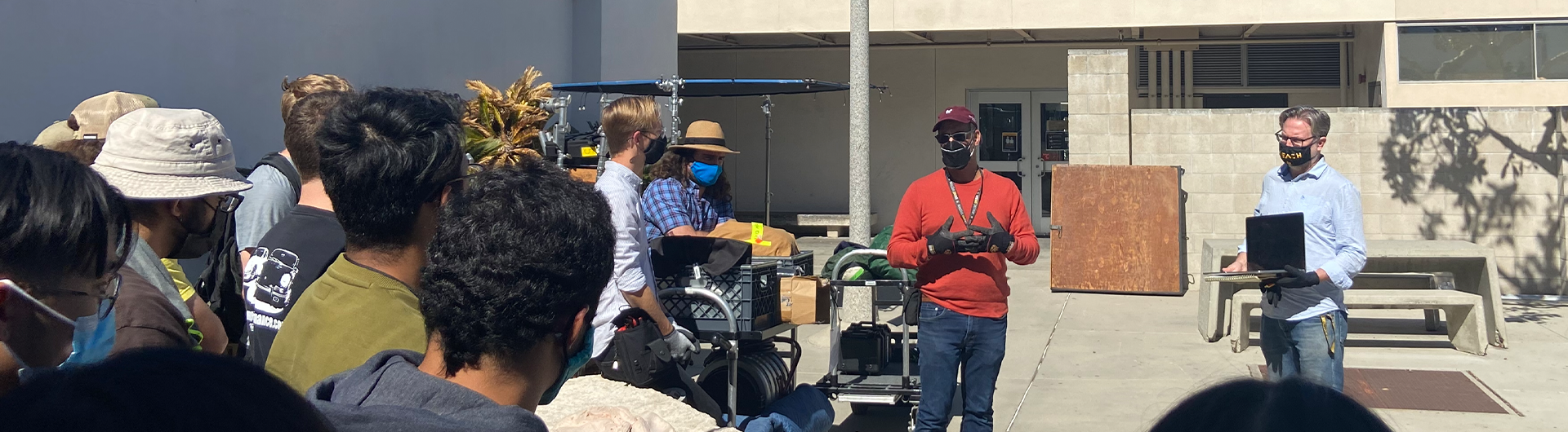 Film students on set outdoors with equipment listening to instruction by film professors 