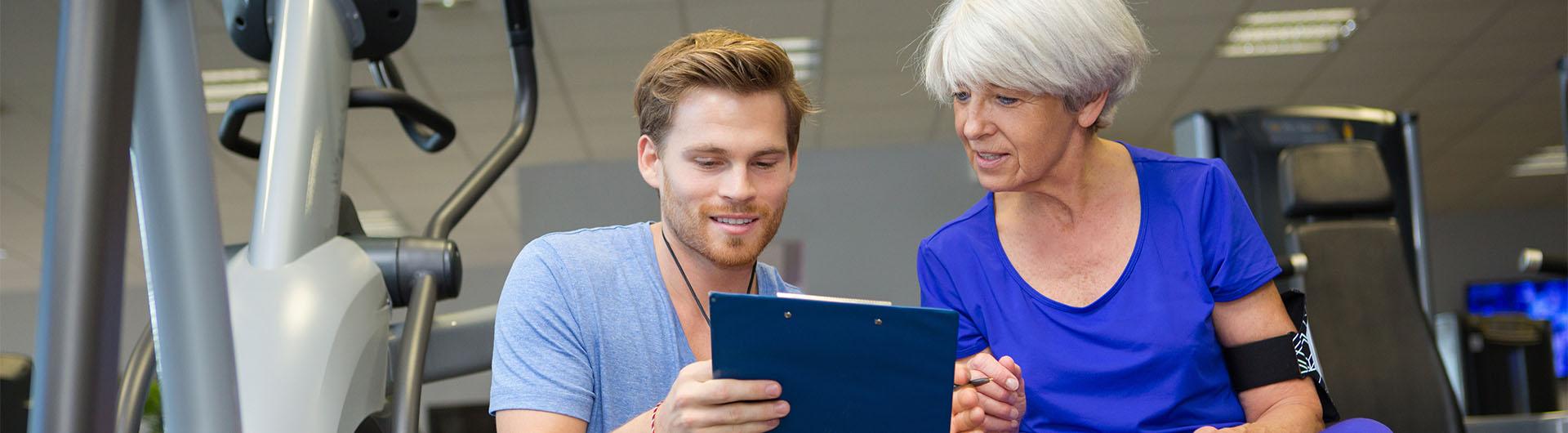 Personal trainer with clipboard helping elderly woman