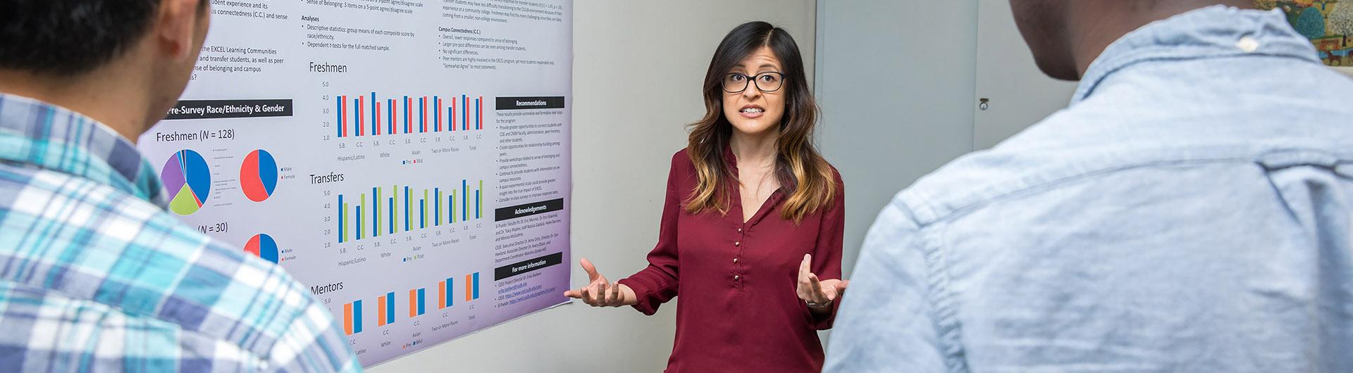 Instructor in front of data poster talking to two students